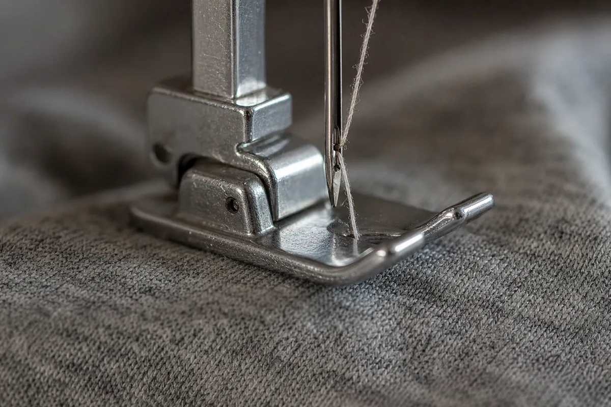 Aiguille de machine à coudre et pied presseur posés sur une chute de jersey gris