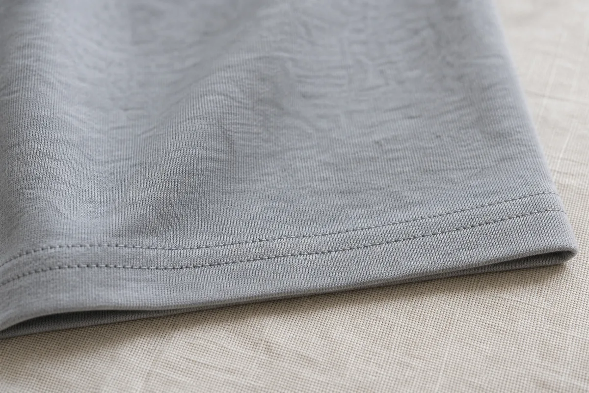 Bas de t-shirt en jersey terminé par un ourlet à double surpiqûre, posé à plat sur un lin clair